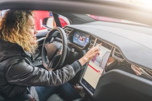 Young woman sits behind wheel in car and uses an electronic dashboard, tablet computer. Girl is traveler looking for a way through navigation system. Trip, caravanning, tourism, journey.