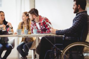 man in wheelchair smiling with other co-workers talking in the office table