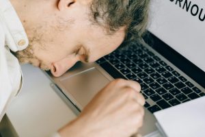 tired employee asleep with his head resting on a laptop