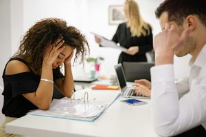 woman in a business meeting, holding her head in her hands, looking stressed